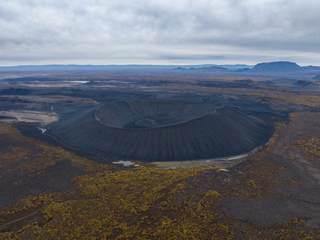 Aerial view of the stark dark volcanic crater contrasting against the golden autumn vegetation under a cloudy sky Myvatn &THORN;ingeyjarsveit Iceland.