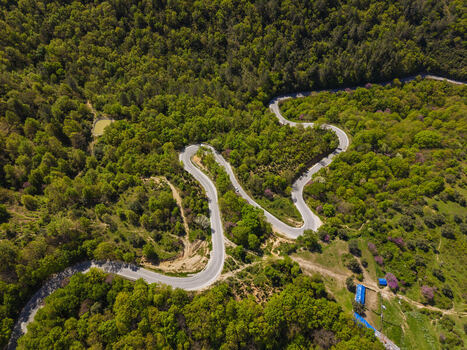 Aerial view of the winding road of Muzine Pass surrounded by dense green forests and lush vegetation in the mountainous landscape of Muzina Qarku i Vlores Albania. Aerial view of the winding road of Muzine Pass surrounded by dense green forests and lush vegetation in the mountainous landscape of Muzina Qarku i Vlores Albania.