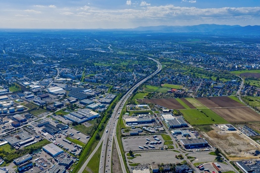 Aerial view of the stark contrast between the industrial buildings and the lush green fields bisected by a snaking highway Sausheim Grand Est France.