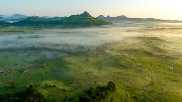 Aerial view of the lush green landscape of Igatpuri with rolling hills misty fields and morning light in Igatpuri Maharashtra India.