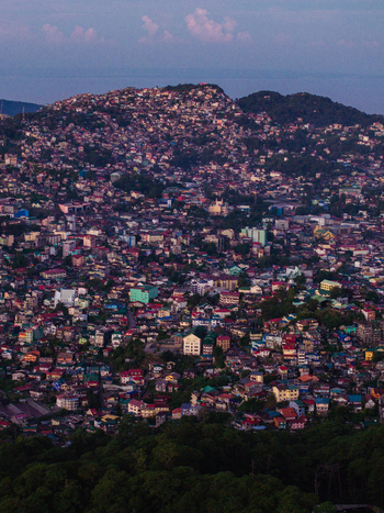 Aerial view of dense colorful houses on rolling hillsides under a twilight sky with lush green trees in Baguio Cordillera Administrative Region Philippines.