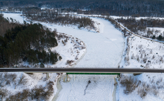 Aerial view of a bridge crossing a frozen river surrounded by snow covered forests and winter landscape Lithuania. Aerial view of a bridge crossing a frozen river surrounded by snow covered forests and winter landscape Lithuania.