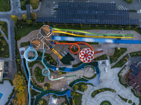 Aerial view of a colorful water park featuring winding slides a circular pool and a lazy river surrounded by landscaped grounds and buildings with solar panels in Bulgaria. Aerial view of a colorful water park featuring winding slides a circular pool and a lazy river surrounded by landscaped grounds and buildings with solar panels in Bulgaria.