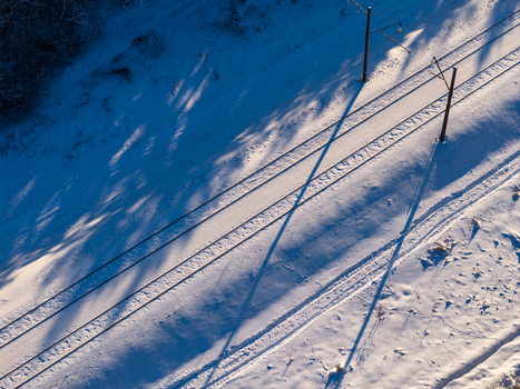 Aerial view of railway tracks covered in fresh snow with long tree shadows and power line poles during winter in Lithuania. Aerial view of railway tracks covered in fresh snow with long tree shadows and power line poles during winter in Lithuania.