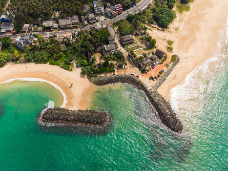 Aerial view of the tropical coastline with stone breakwaters sandy beaches and lush palm trees lining the shore in Peraliya Southern Province Sri Lanka. Aerial view of the tropical coastline with stone breakwaters sandy beaches and lush palm trees lining the shore in Peraliya Southern Province Sri Lanka.