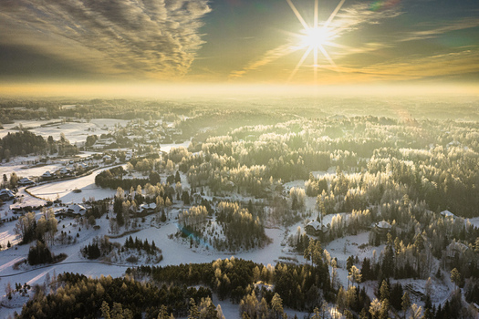 Aerial view of the eco village of Amatciems in winter with snow covered forests frozen ponds and wooden houses under golden hour light in Amatciems Cesu novads Latvia. Aerial view of the eco village of Amatciems in winter with snow covered forests frozen ponds and wooden houses under golden hour light in Amatciems Cesu novads Latvia.