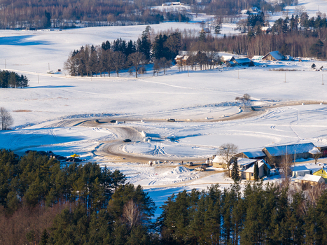 Aerial view of a winding snowy track with cars driving through a winter landscape with pine forests and rural houses Moletai Utena County Lithuania.