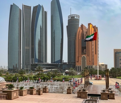 View of modern skyscrapers and a waving UAE flag overlooking a plaza with fountains palm trees and people in Abu Dhabi Abu Dhabi United Arab Emirates. View of modern skyscrapers and a waving UAE flag overlooking a plaza with fountains palm trees and people in Abu Dhabi Abu Dhabi United Arab Emirates.