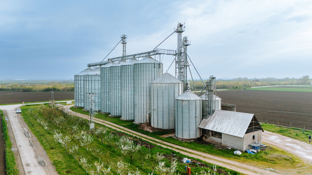 Aerial view of gleaming silver grain silos stand tall amidst the agricultural landscape reflecting the overcast sky Sremska Mitrovica Vojvodina Serbia. Aerial view of gleaming silver grain silos stand tall amidst the agricultural landscape reflecting the overcast sky Sremska Mitrovica Vojvodina Serbia.