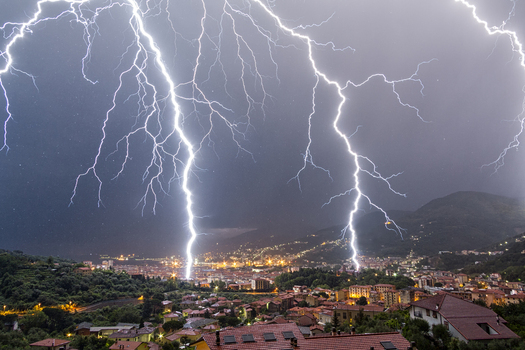 View of powerful lightning bolts striking over the city skyline and rooftops at night in La Spezia Liguria Italy. View of powerful lightning bolts striking over the city skyline and rooftops at night in La Spezia Liguria Italy.