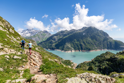 View of hikers on a mountain trail overlooking the turquoise Lac d Emosson near the VerticAlp Emosson attraction in Le Chatelard Fribourg Switzerland. View of hikers on a mountain trail overlooking the turquoise Lac d Emosson near the VerticAlp Emosson attraction in Le Chatelard Fribourg Switzerland.