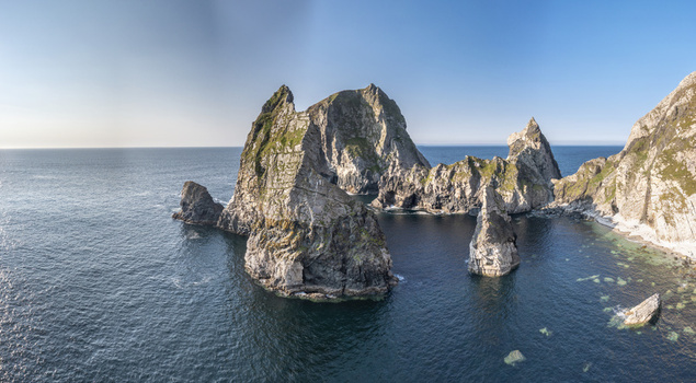 Aerial view of Glenlough Bay featuring dramatic sea stacks rugged cliffs and deep blue Atlantic waters under a clear sky in Ardara County Donegal Ireland.