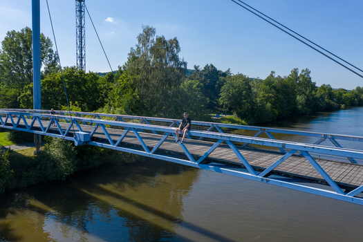 Aerial view of a man sitting on the railing of a blue pedestrian bridge over the Regnitz river surrounded by lush green trees Forchheim Bayern Germany.