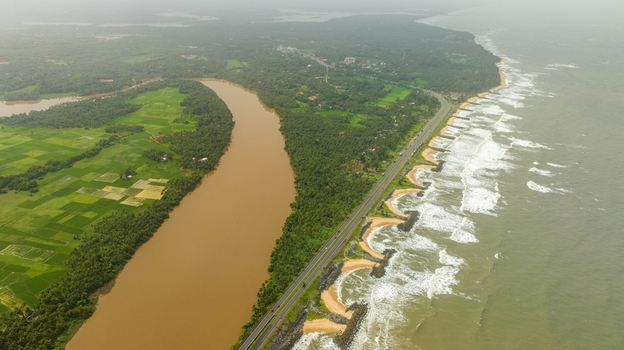 Aerial view of Maravanthe beach with a highway separating the Arabian Sea and Souparnika River surrounded by lush green fields and coconut trees in Maravanthe Karnataka India. Aerial view of Maravanthe beach with a highway separating the Arabian Sea and Souparnika River surrounded by lush green fields and coconut trees in Maravanthe Karnataka India.