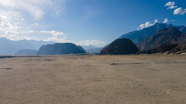 Aerial view of Sarfaranga Cold Desert Shigar with vast sandy plains tire tracks and rugged mountain ranges under a clear blue sky in Skardu Gilgit Pakistan.