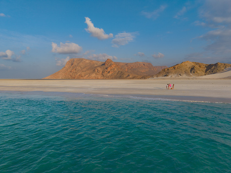 Aerial view of turquoise waters meet the pristine white sands of Qalansiyah Beach framed by the rugged sun kissed mountains Qalanciya lagoon Socotra Yemen.