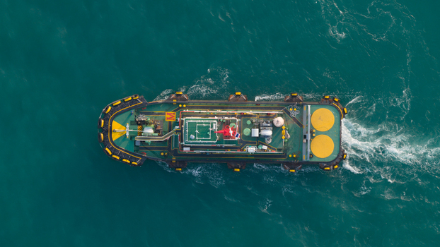 Aerial view of a tugboat navigating through turquoise waters with a white wake near the port of Laem Chabang Chon Buri Thailand.