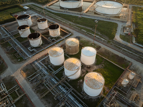 Aerial view of industrial oil storage tanks and complex pipeline networks surrounded by green fields during sunset in Augusta Sicily Italy. Aerial view of industrial oil storage tanks and complex pipeline networks surrounded by green fields during sunset in Augusta Sicily Italy.