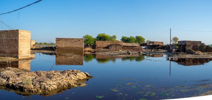 View of flooded rural landscape with partially submerged brick houses and calm water reflecting the clear blue sky in Jacobabad Sindh Pakistan.