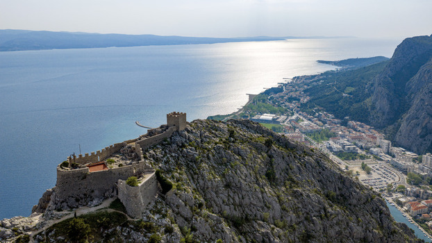 Aerial view of the historic Starigrad Fortress perched on a rugged mountain ridge overlooking the coastal town and the blue Adriatic Sea in Omis Split Dalmatia County Croatia. Aerial view of the historic Starigrad Fortress perched on a rugged mountain ridge overlooking the coastal town and the blue Adriatic Sea in Omis Split Dalmatia County Croatia.
