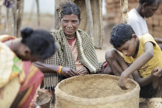 Odisha India 26 March 2026 View of a woman with a nose ring and shawl sitting with a child a woven basket between them amidst the rural landscape. Odisha India 26 March 2026 View of a woman with a nose ring and shawl sitting with a child a woven basket between them amidst the rural landscape.