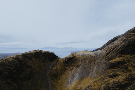 Aerial view of the rugged slopes of Bla Bheinn mountain with rocky terrain under an overcast sky in Isle of Skye Scotland United Kingdom. Aerial view of the rugged slopes of Bla Bheinn mountain with rocky terrain under an overcast sky in Isle of Skye Scotland United Kingdom.