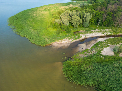 Aerial view of the river mouth flowing into the lake surrounded by lush green reeds and dense forest along the shoreline in Tolkmicko Warmian Masurian Voiv Poland. Aerial view of the river mouth flowing into the lake surrounded by lush green reeds and dense forest along the shoreline in Tolkmicko Warmian Masurian Voiv Poland.