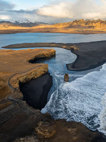 Aerial view of Dyrholaey featuring dramatic black sand beaches rugged cliffs and crashing waves under a soft sky in Myrdalshreppur Iceland. Aerial view of Dyrholaey featuring dramatic black sand beaches rugged cliffs and crashing waves under a soft sky in Myrdalshreppur Iceland.