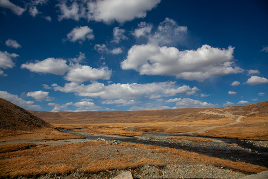 View of Deosai National Park featuring a winding stream through golden alpine meadows under a bright blue sky with scattered clouds in Astore Gilgit Pakistan. View of Deosai National Park featuring a winding stream through golden alpine meadows under a bright blue sky with scattered clouds in Astore Gilgit Pakistan.