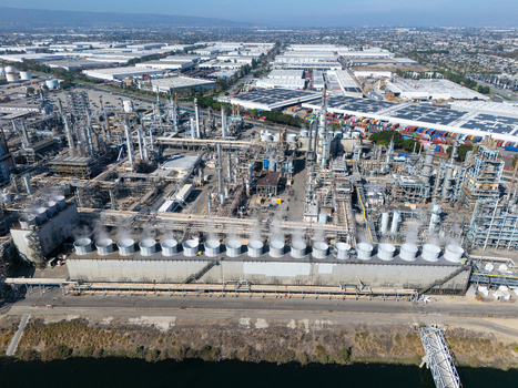 Aerial view of an industrial oil refinery featuring large cooling towers complex piping systems and storage tanks in an urban industrial zone in Carson California United States.