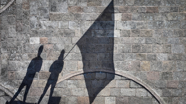 Aerial view of stark shadows cast by figures and a flag against the textured stone wall of Barnenez Cairn Plouezoc h Bretagne France. Aerial view of stark shadows cast by figures and a flag against the textured stone wall of Barnenez Cairn Plouezoc h Bretagne France.