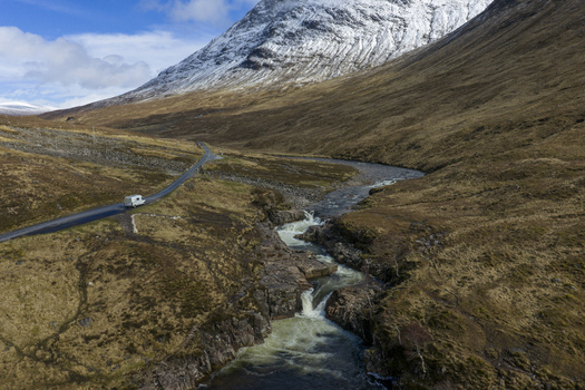 Aerial view of Glen Etive Waterfall View Point with a winding river and a white van on the road against snow capped mountains in Ballachulish Scotland United Kingdom.