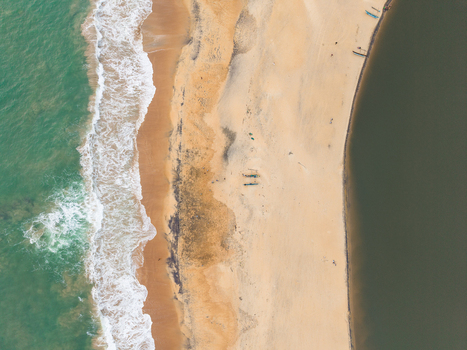 Aerial view of a sandy beach strip separating turquoise ocean waves from a calm dark lagoon with small fishing boats Galle Southern Province Sri Lanka.