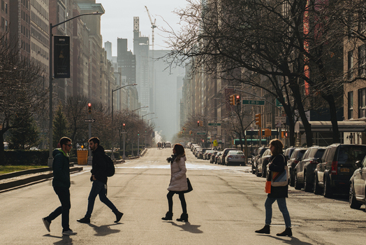 New York United States 13 April 2015 View of people crossing a street in New York City with urban buildings parked cars and bare trees under soft daylight.