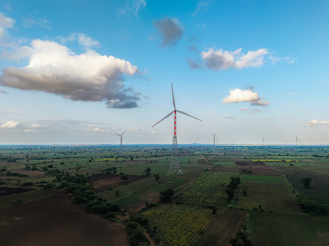 Aerial view of a wind turbine standing in a rural landscape with agricultural fields under a blue sky with scattered clouds in Hampi Karnataka India.