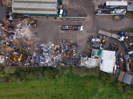 Aerial view of a bustling junkyard with heavy machinery amidst scattered debris juxtaposed against a serene green field Stafford England United Kingdom. Aerial view of a bustling junkyard with heavy machinery amidst scattered debris juxtaposed against a serene green field Stafford England United Kingdom.