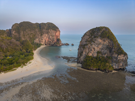 Aerial view of rugged limestone cliffs meet the turquoise sea fringed by a golden beach Ao Nang Thailand.