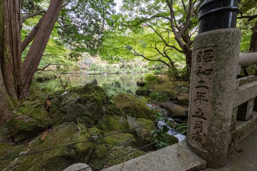 View of mossy stones and lush greenery reflecting in tranquil waters under the canopy of trees with a stone pillar in the foreground Narita Chiba Japan. View of mossy stones and lush greenery reflecting in tranquil waters under the canopy of trees with a stone pillar in the foreground Narita Chiba Japan.