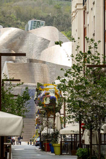 View of the Guggenheim Museum Bilbao with its titanium curves and the Puppy floral sculpture seen from a street with trees and buildings in Bilbao Euskadi Spain. View of the Guggenheim Museum Bilbao with its titanium curves and the Puppy floral sculpture seen from a street with trees and buildings in Bilbao Euskadi Spain.