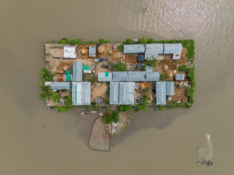 Mithamain Upazila Bangladesh 09 May 2026 Aerial view of a small island village with tin roofed houses and green trees surrounded by the vast waters of the haor region.