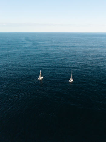 Aerial view of two sailboats sailing on the deep blue ocean in Dee Why New South Wales Australia. Aerial view of two sailboats sailing on the deep blue ocean in Dee Why New South Wales Australia.