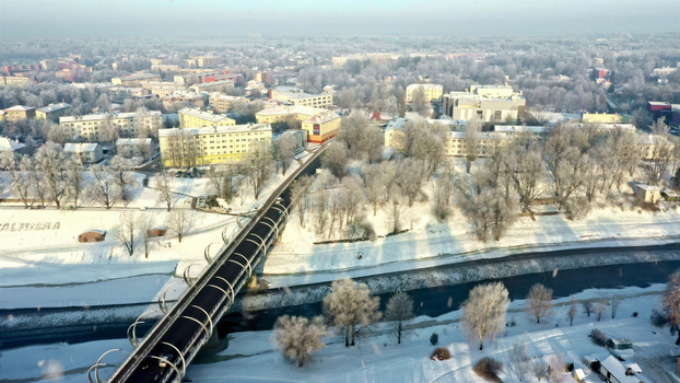 Aerial view of a modern bridge spanning a river in a snow covered town with frost covered trees and residential buildings in Latvija. Aerial view of a modern bridge spanning a river in a snow covered town with frost covered trees and residential buildings in Latvija.
