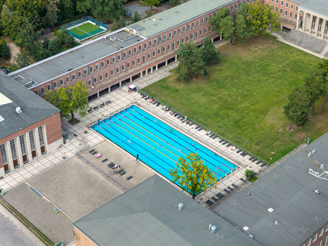 Berlin Germany 26 September 2026 Aerial view of the Olympiastadion Berlin swimming pool featuring a bright blue lap pool surrounded by sun loungers lawns and historic brick architecture.