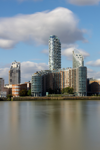 View of Greenwich skyline with modern residential towers and glass buildings reflecting in the calm River Thames under a blue sky London England United Kingdom. View of Greenwich skyline with modern residential towers and glass buildings reflecting in the calm River Thames under a blue sky London England United Kingdom.