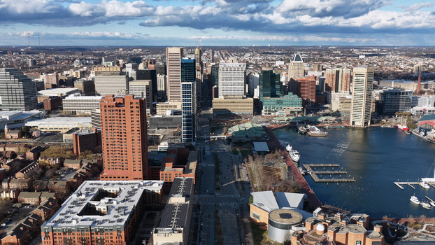 Aerial view of Inner Harbor Baltimore featuring modern skyscrapers waterfront docks with boats and urban architecture under a cloudy blue sky in Baltimore Maryland United States.
