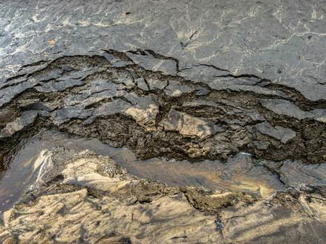 Aerial view of cracked dark soil and mud with a small stream flowing through the eroded landscape in Latvia. Aerial view of cracked dark soil and mud with a small stream flowing through the eroded landscape in Latvia.