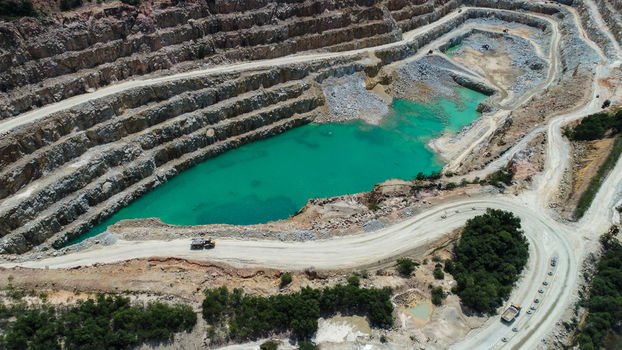 Aerial view of a gravel and sand mine on Karimun Island featuring terraced rock walls a turquoise water filled pit and mining trucks on dirt roads in Karimun Kepulauan Riau Indonesia.