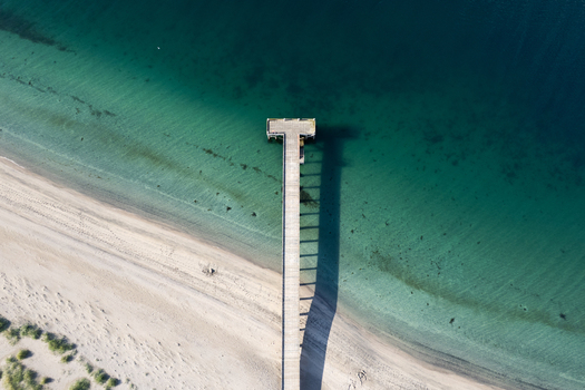 Aerial view of Onundarfjordur Pier extending from a sandy beach into clear turquoise water with a long shadow Holt Isafjardabaer Iceland. Aerial view of Onundarfjordur Pier extending from a sandy beach into clear turquoise water with a long shadow Holt Isafjardabaer Iceland.