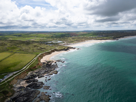 Aerial view of Godrevy Beach with turquoise waves crashing against rocky cliffs and green coastal fields under a cloudy sky in Gwithian England United Kingdom. Aerial view of Godrevy Beach with turquoise waves crashing against rocky cliffs and green coastal fields under a cloudy sky in Gwithian England United Kingdom.