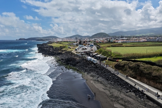 Aerial view of Praia do Areal de Santa Barbara featuring dark volcanic sand crashing Atlantic waves and a coastal promenade with people Ribeira Grande Acores Portugal. Aerial view of Praia do Areal de Santa Barbara featuring dark volcanic sand crashing Atlantic waves and a coastal promenade with people Ribeira Grande Acores Portugal.